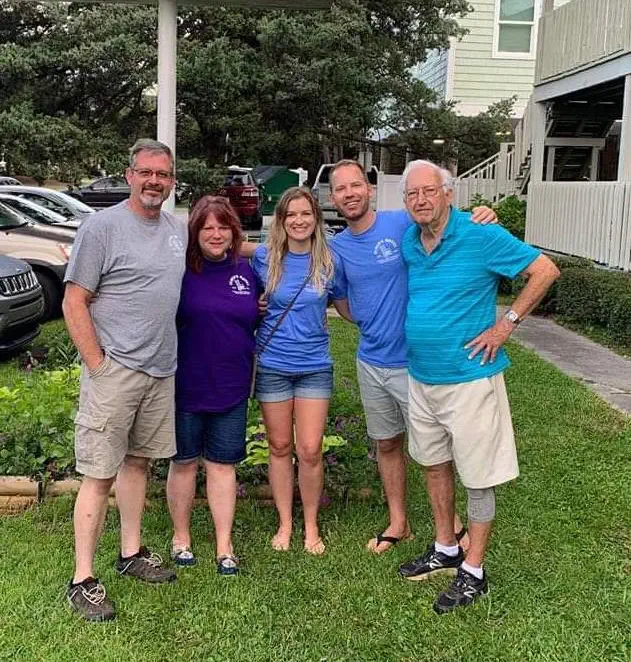 Five smiling people posing together outdoors on grass