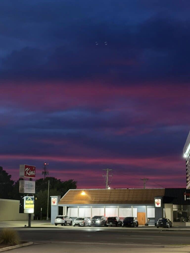 Vibrant purple and pink sunset over roadside commercial strip